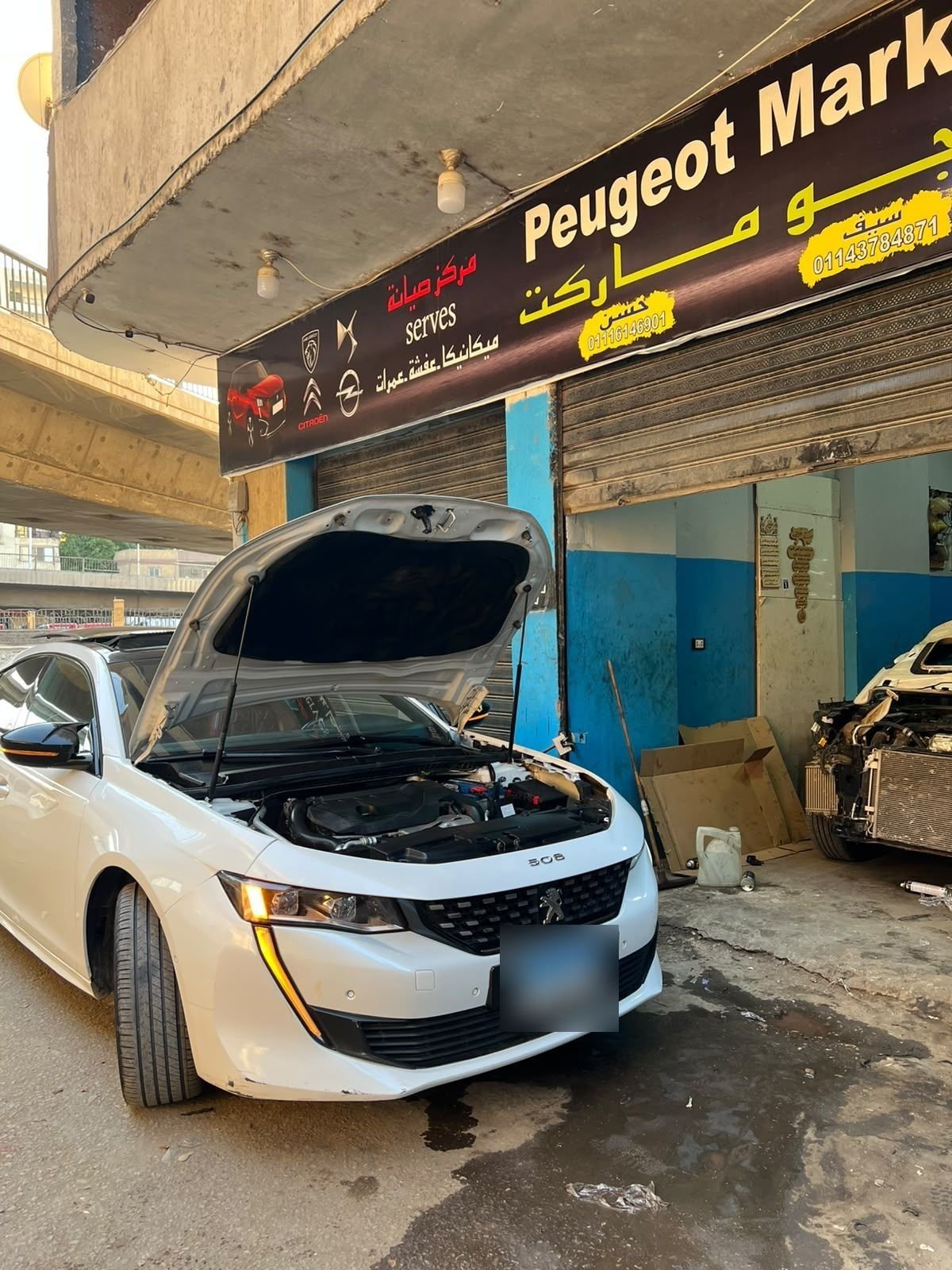 A white Peugeot 508 with its bonnet open under the Peugeot Market sign.