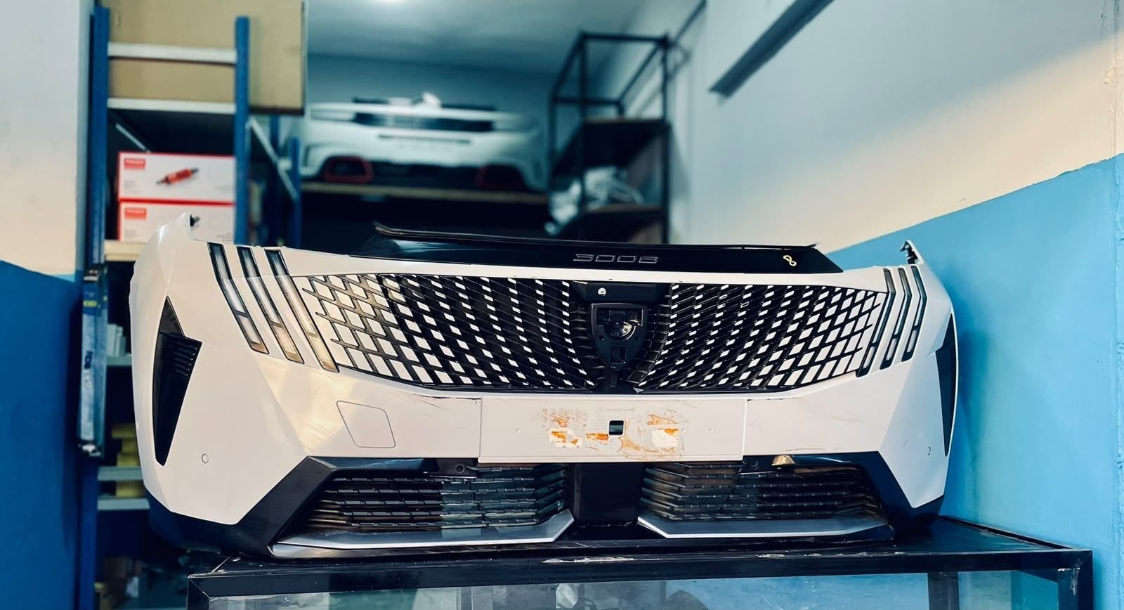 A white front bumper for the new Peugeot 3008 on a stand inside the workshop.